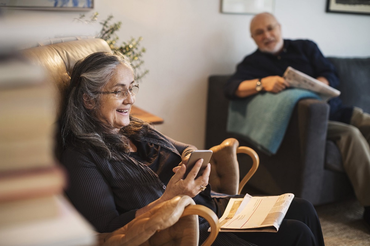 starsza kobieta z telefonem na kanapie, dalej starszy mężczyzna na krześle